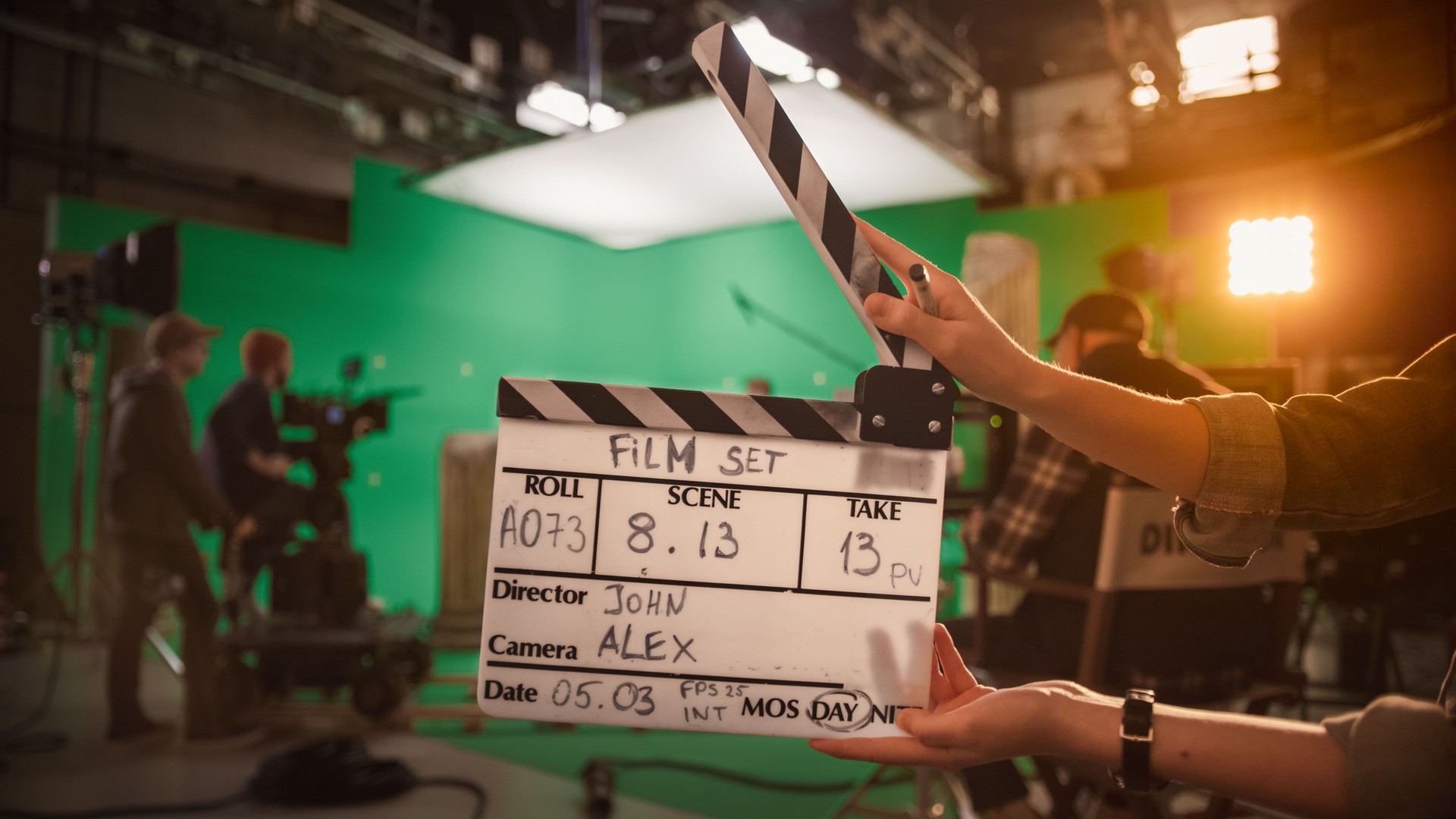 On Film Studio Set Camera Assistant Holds Clapperboard. Green Screen Scene with Talented Cameraman in the Background. Close-up Shot.